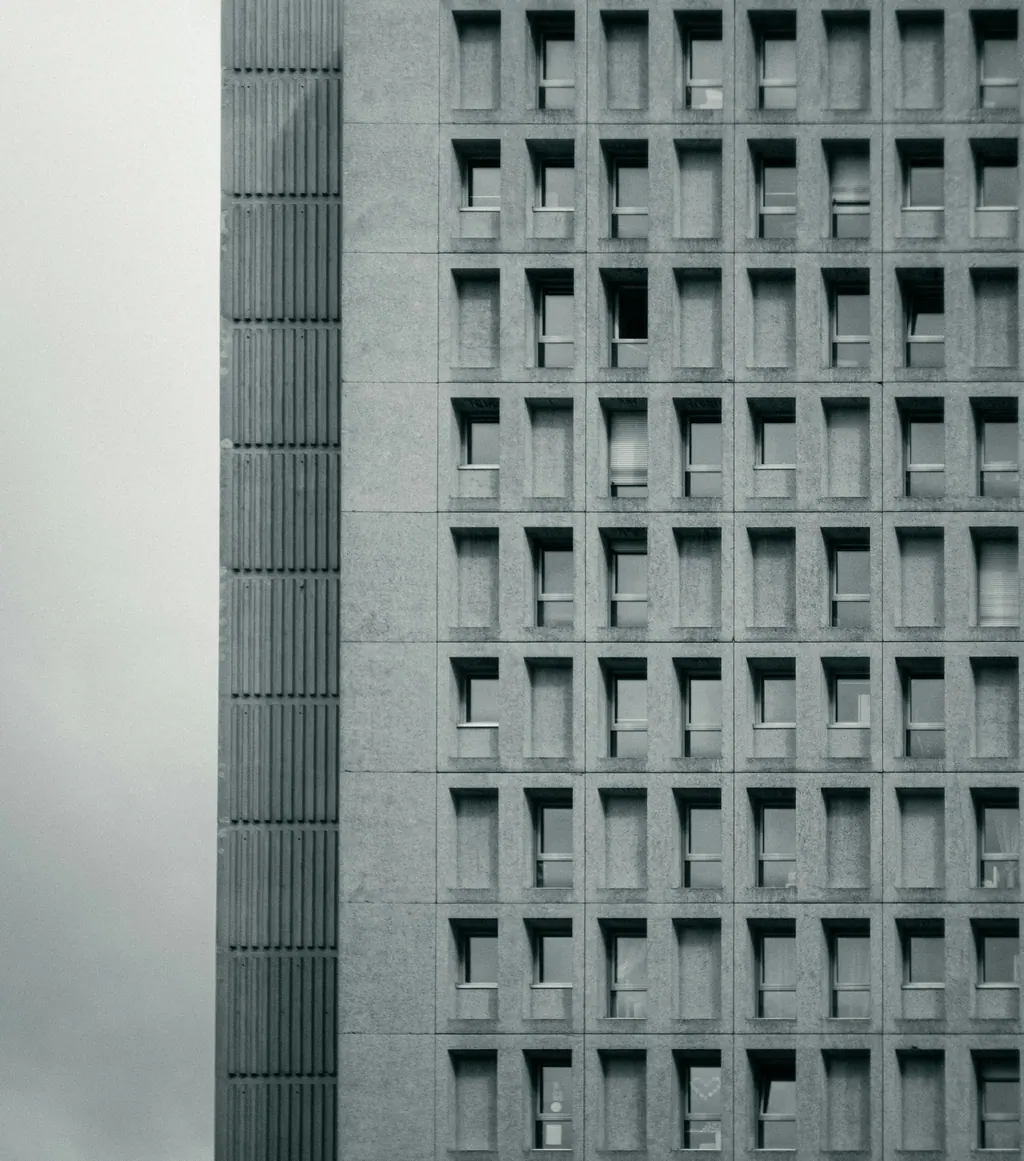 Fachada de concreto brutalista con una retícula de ventanas hundidas, en blanco y negro.